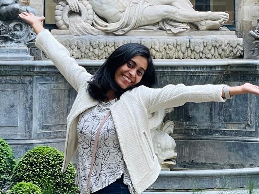 Soumya outside a stone courtyard fountain, arms thrown wide, laughing